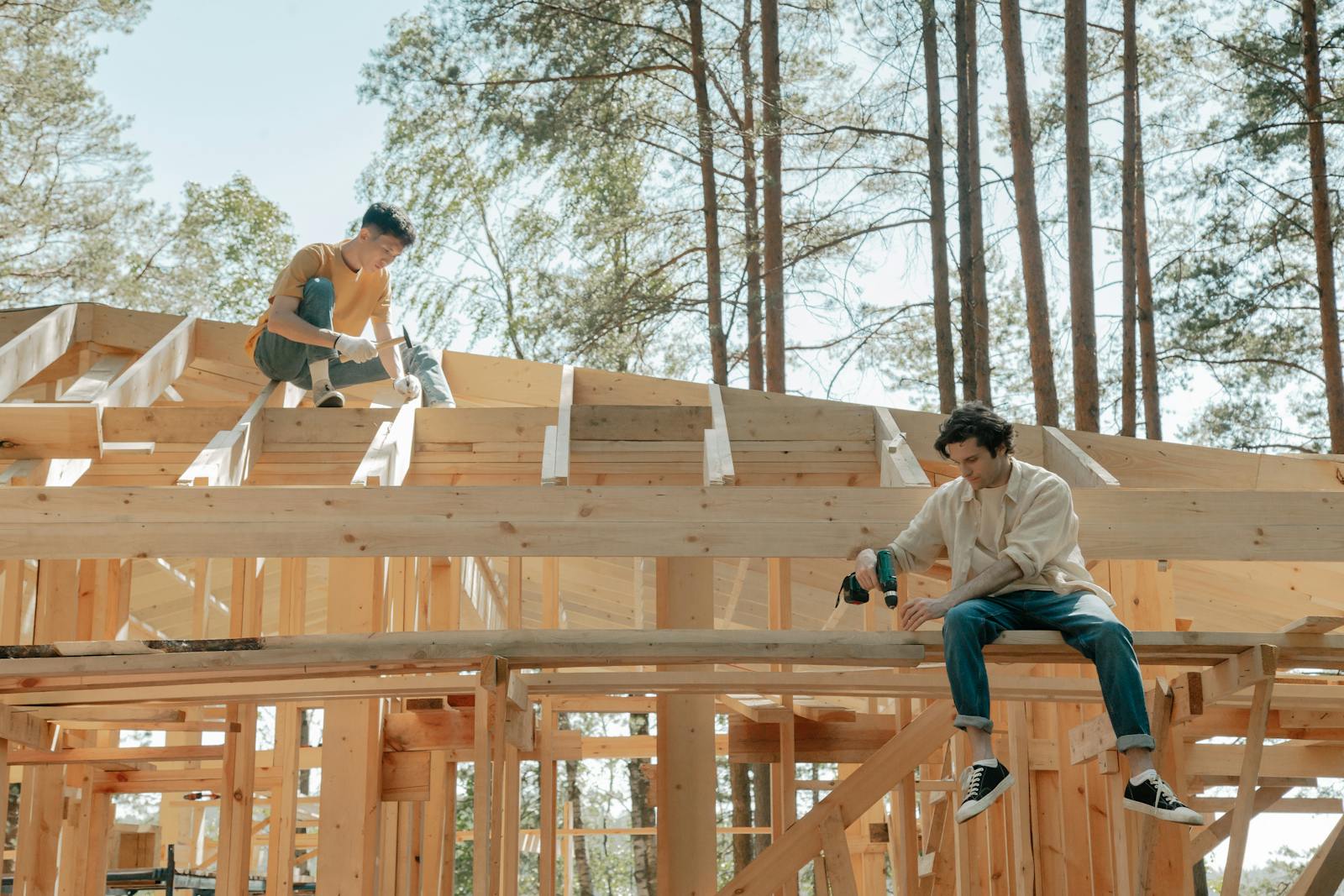 Two male carpenters working on a wooden framework of a house under bright daylight.